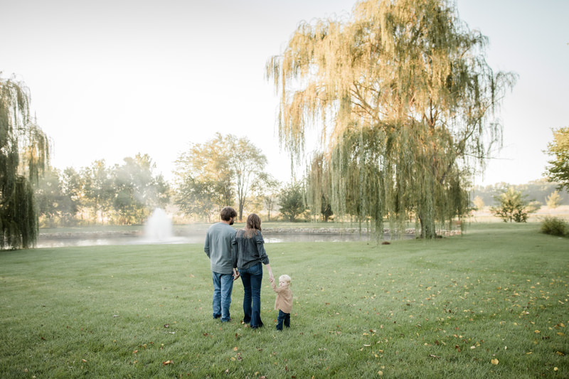 Family of three standing by willow tree at pond