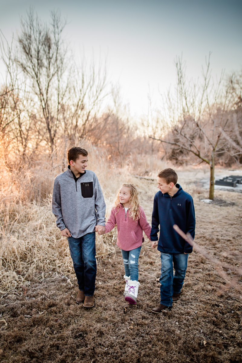 Three siblings walking hand in hand through winter brush at sunset